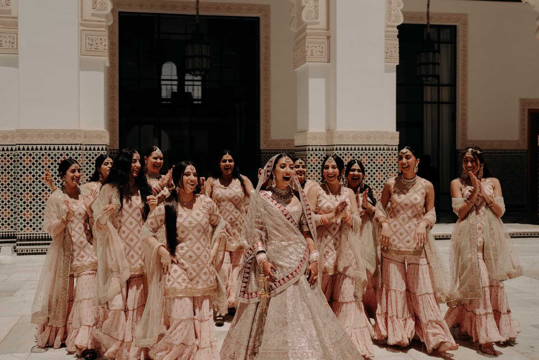 Sikh bride making a happy, surprised expression while surrounded by female friends and family.