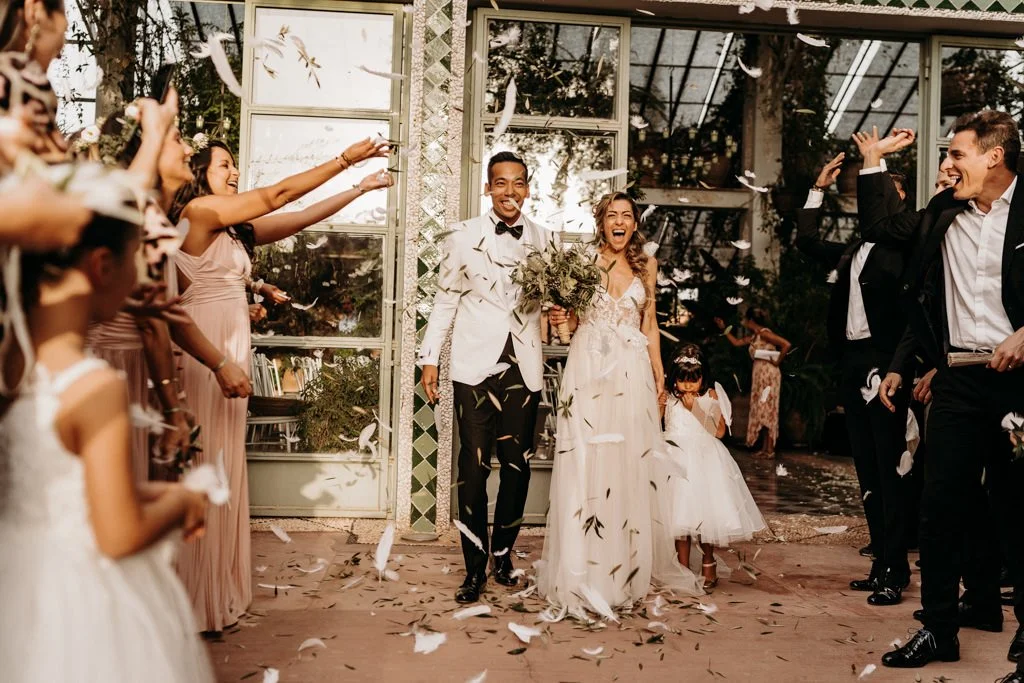 Smiling newlywed couple leaving the ceremony site. Their guests are happy and throw feathers at both of them.