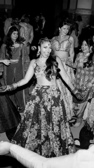 This vibrant scene captures a wedding celebration in Marrakech, with a woman in a white gown and sunglasses surrounded by guests in colorful attire